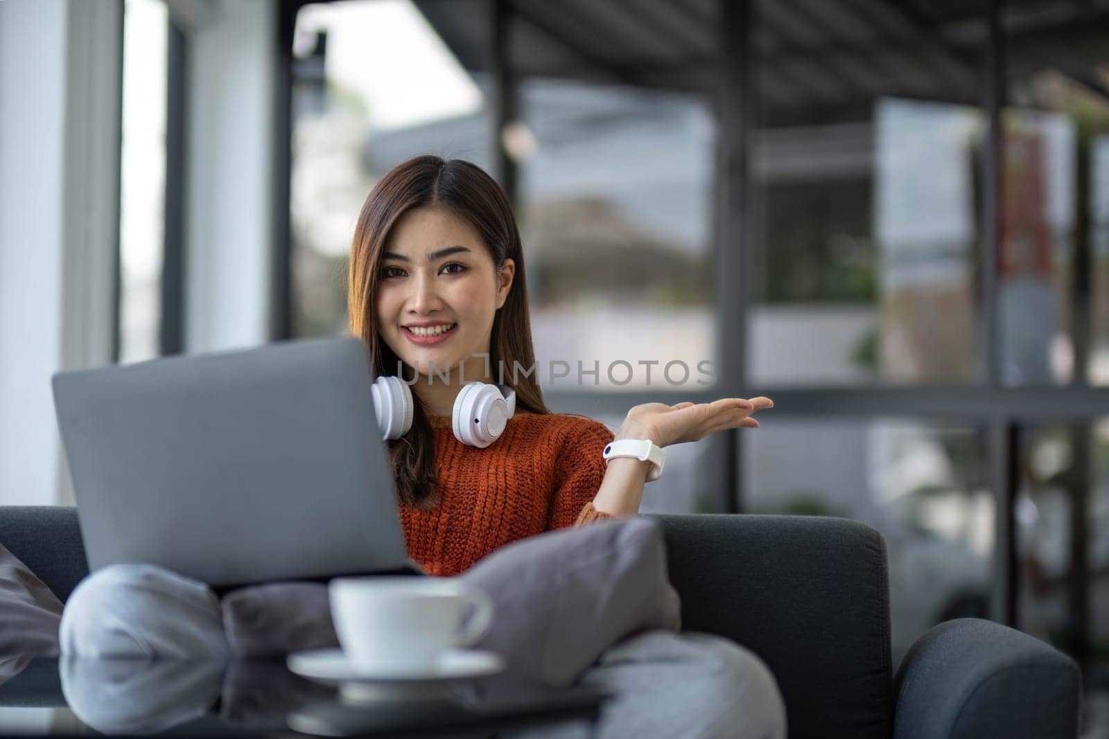 asian young woman listening music with headphone and streaming music from laptop on sofa relaxing at home..