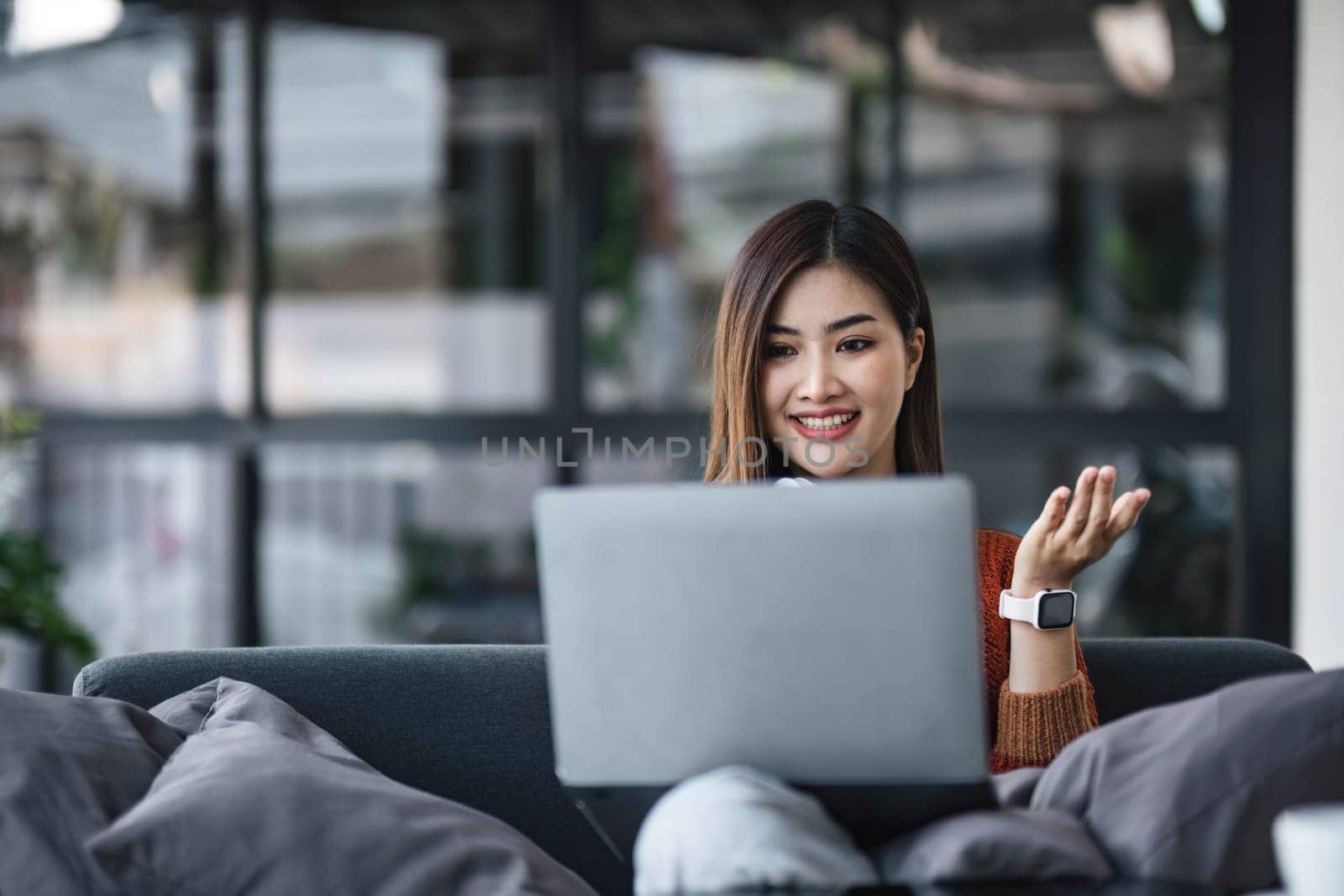 asian young woman listening music with headphone and streaming music from laptop on sofa relaxing at home by wichayada