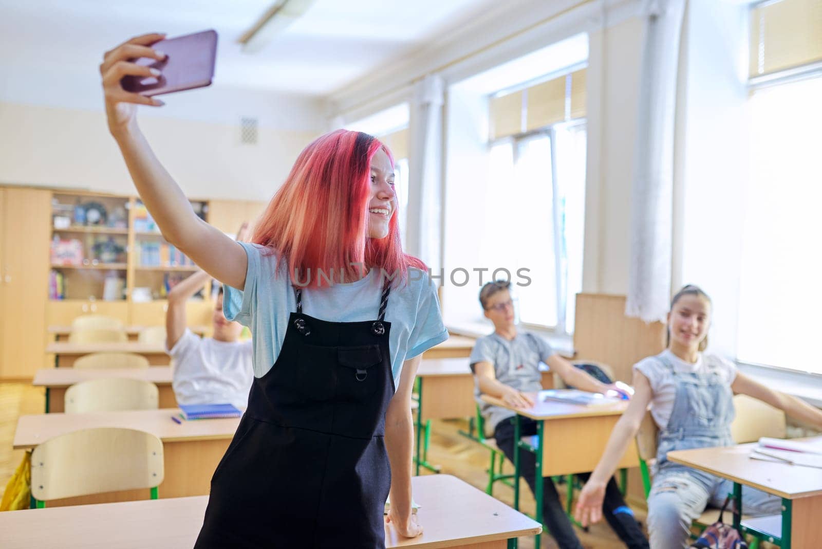 Teenagers students having fun in the classroom, bright trendy girl taking selfie photo with group of classmates friends at school
