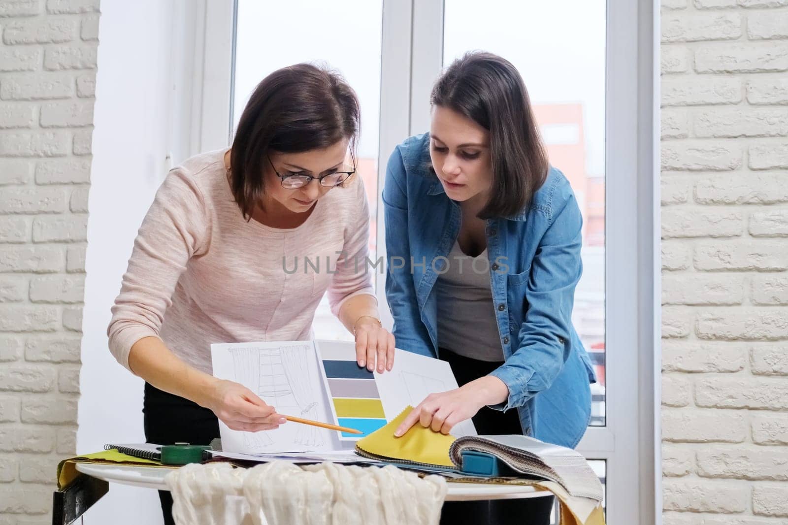 Interior design, two working colleagues designers, or decorator and client choosing curtain fabrics, women looking at samples discussing curtain models