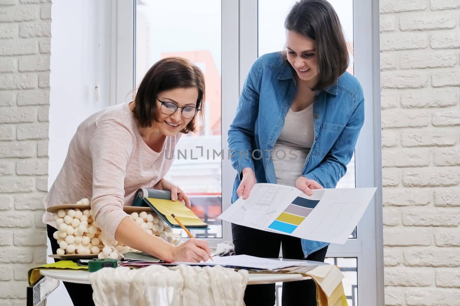 Interior design, two working colleagues designers, or decorator and client choosing curtain fabrics, women looking at samples discussing curtain models