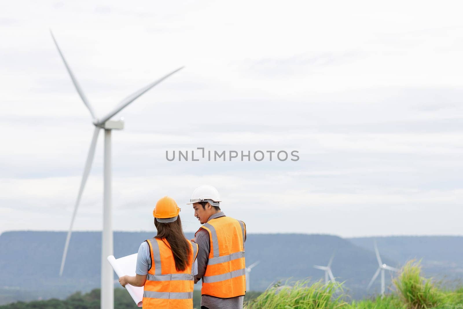 Male and female engineers working on a wind farm atop a hill or mountain in the rural. Progressive ideal for the future production of renewable, sustainable energy.