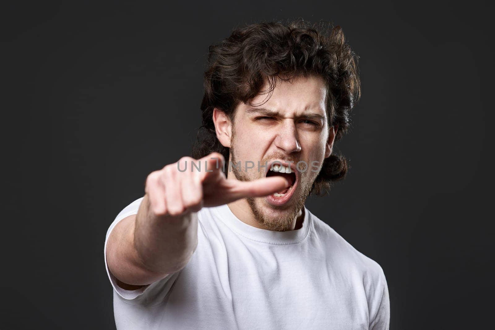 angry caucasian man pointing finger at you and the camera on dark gray background