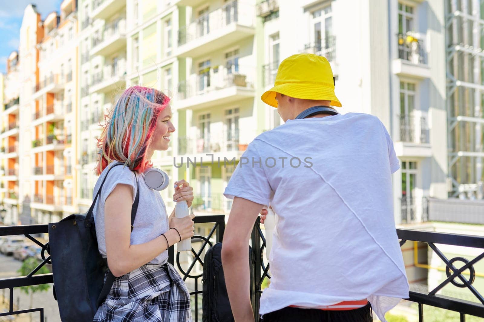 Urban lifestyle of teenagers, couple of college students talking having rest drinking milk drink in bottle outdoors, city street background. Healthy food, youth, recreation and communication concept