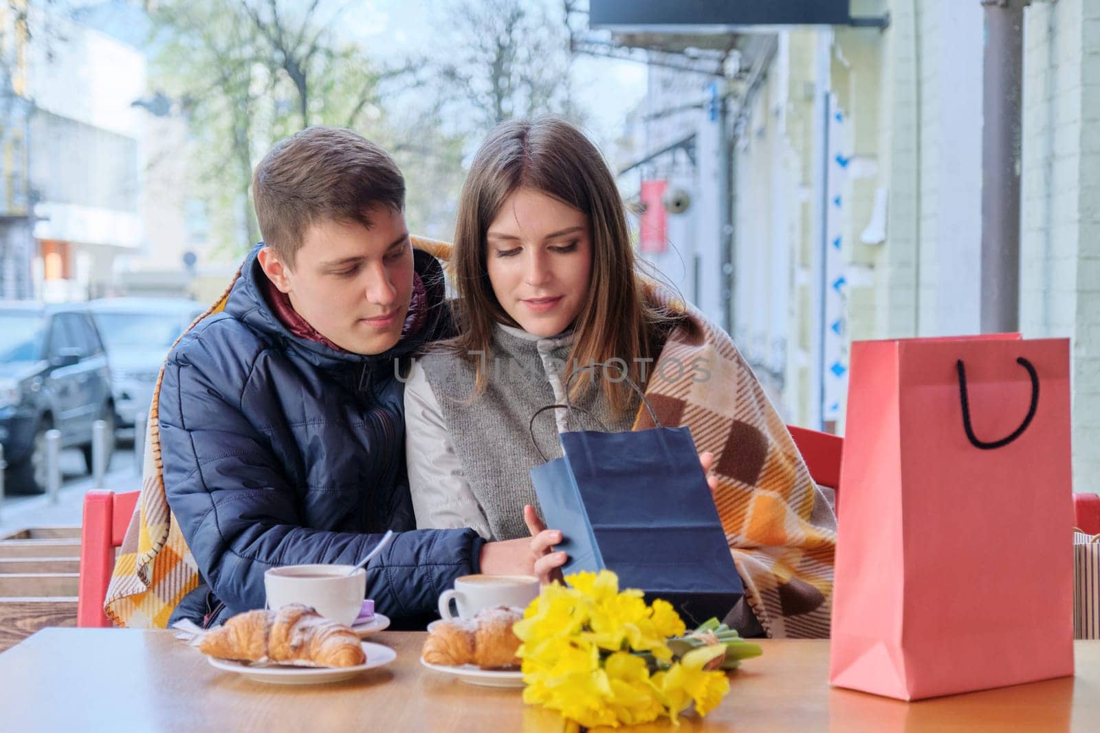 Young couple in outdoor cafe with shopping bags, looking at purchases, drinking coffee