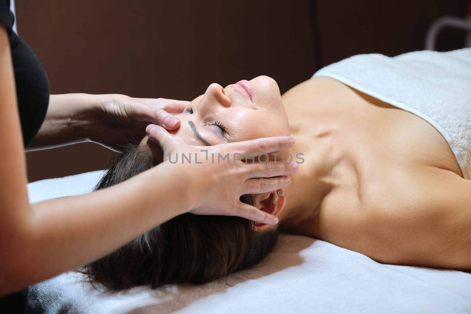 Mature woman face massage, beautician doing facial spa treatments to middle aged client