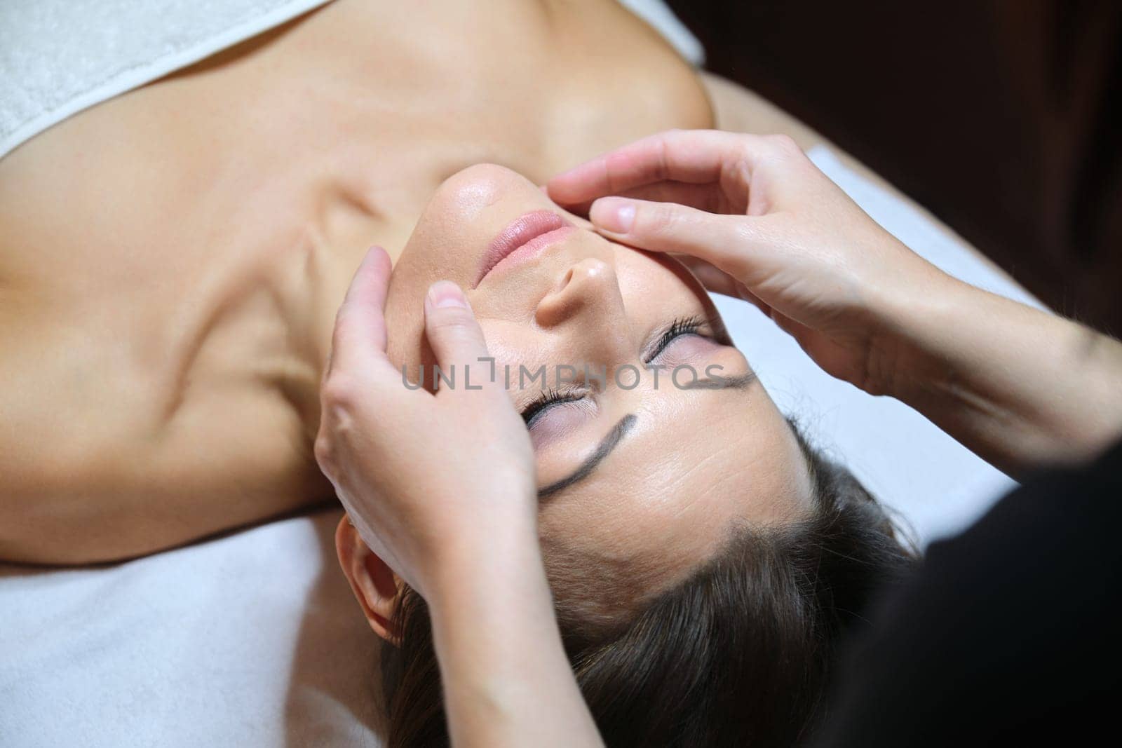 Mature woman face massage, beautician doing facial spa treatments to middle aged client