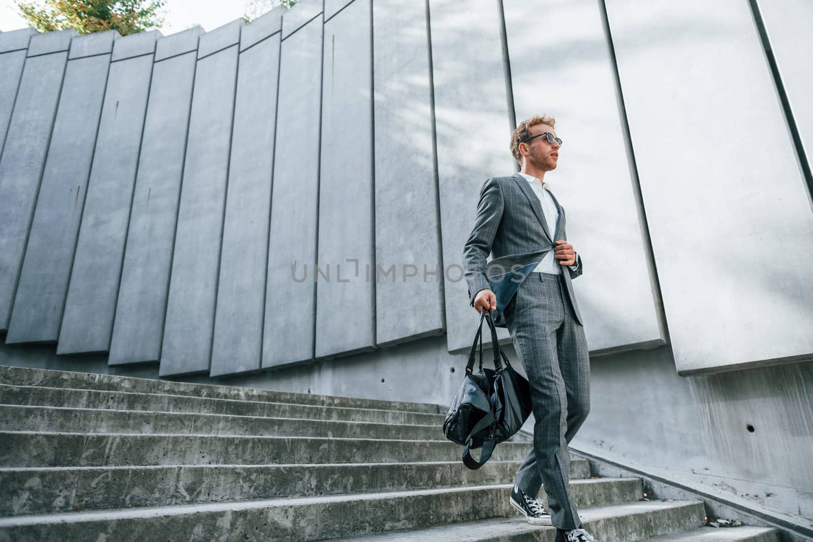 Going down by the stairs. Young businessman in grey formal wear is outdoors in the city.