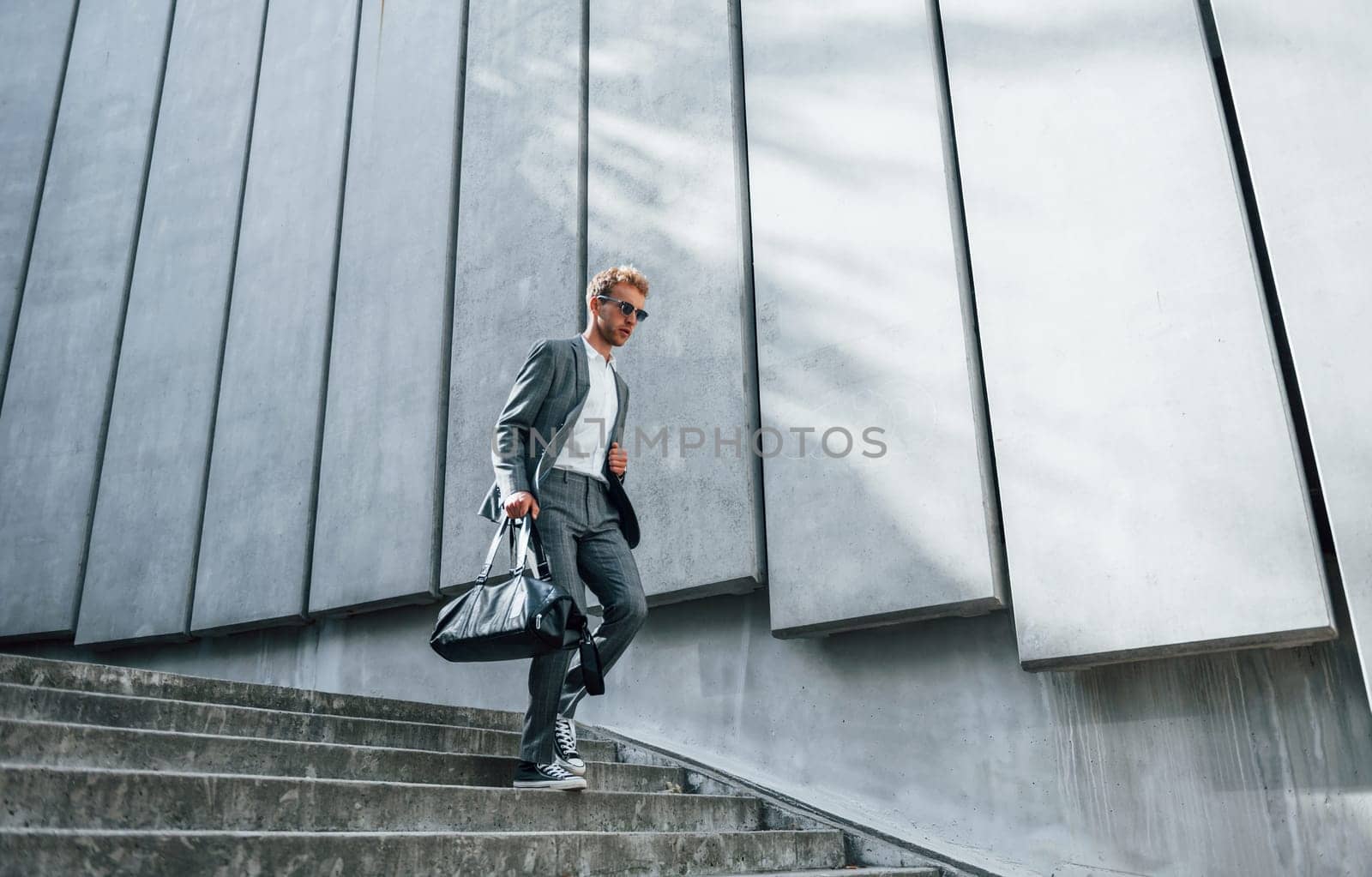 Going down by the stairs. Young businessman in grey formal wear is outdoors in the city by Standret