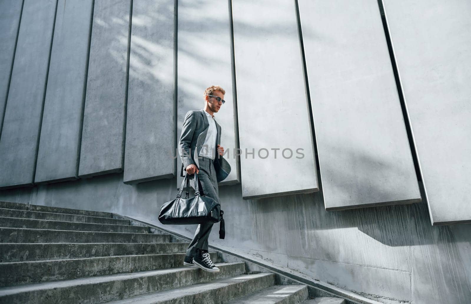 Going down by the stairs. Young businessman in grey formal wear is outdoors in the city.