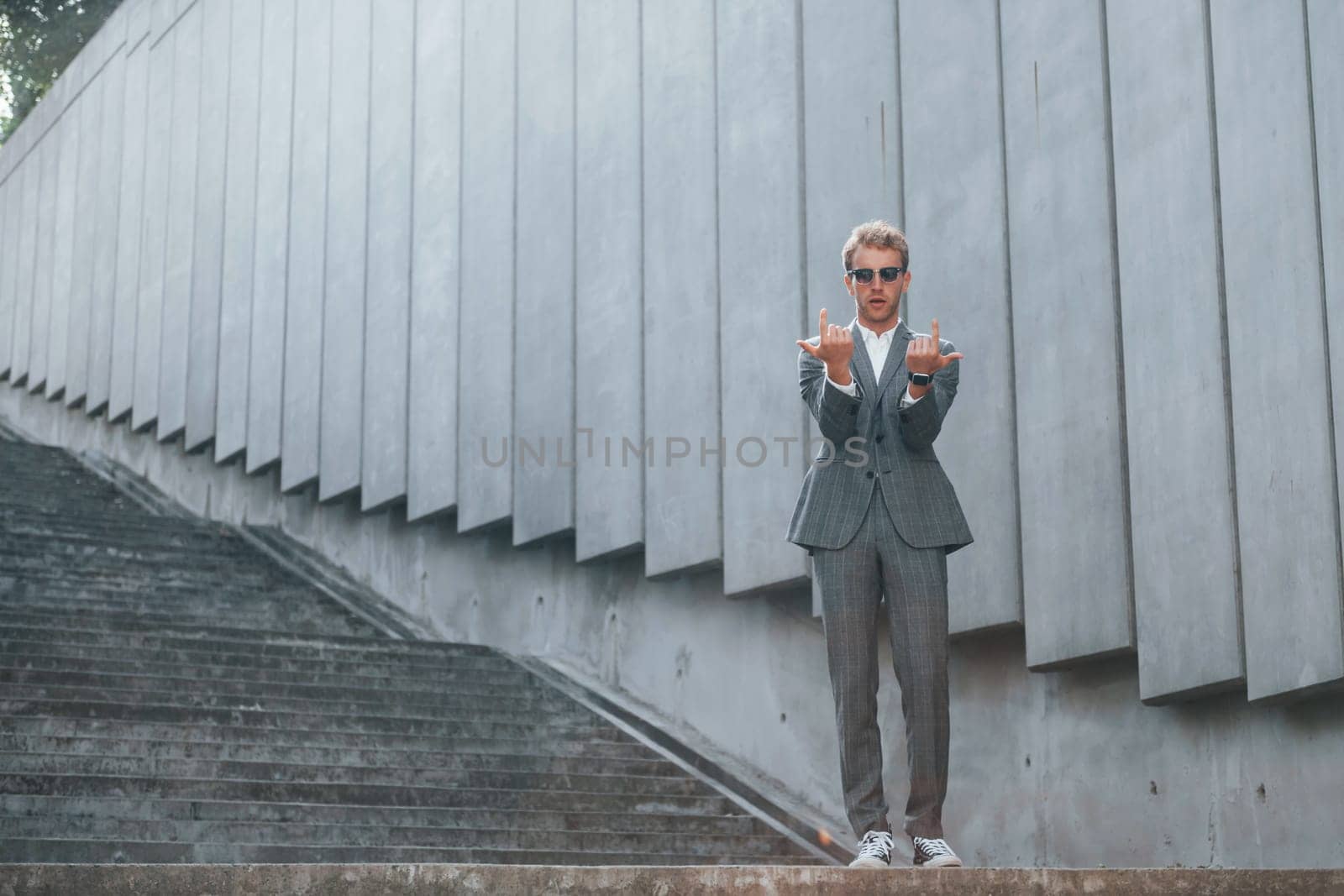 Posing for a camera. Young businessman in grey formal wear is outdoors in the city.