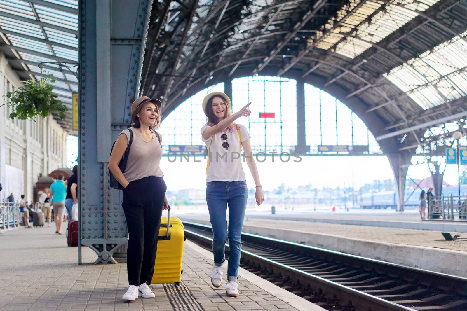 People walking with suitcase at the railway station. Happy mother and teenager daughter traveling with luggage together. Transport, tourism, moving, family concept
