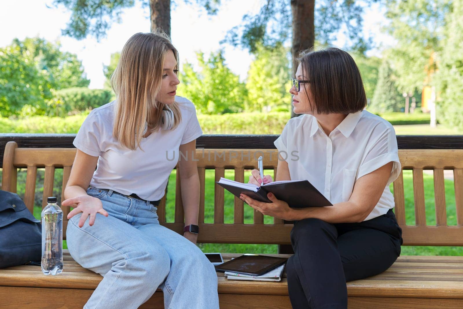 Woman teacher and girl student teenager sitting on the bench in park by VH-studio