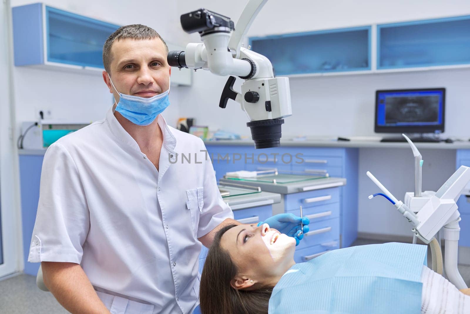 Healthcare dentistry medicine, male doctor dentist treating teeth to a woman patient in chair using dental equipment, tools and microscope, clinic office interior background