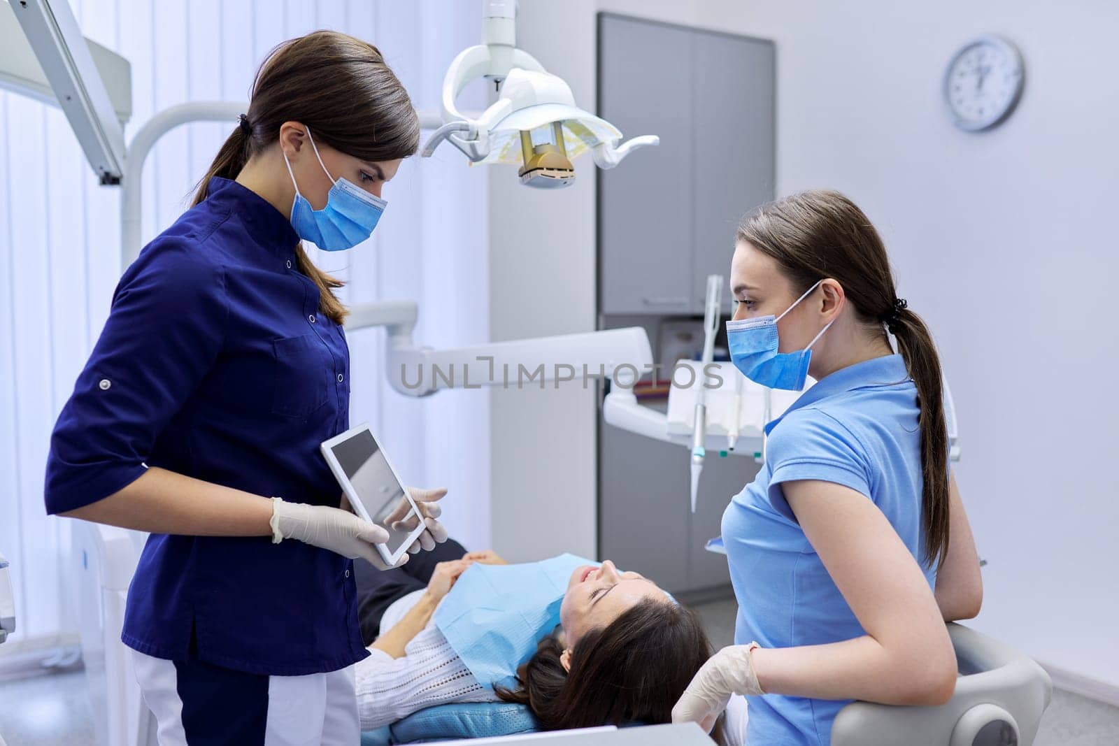 Dentistry, woman patient in chair, doctor colleagues looking in digital tablet by VH-studio