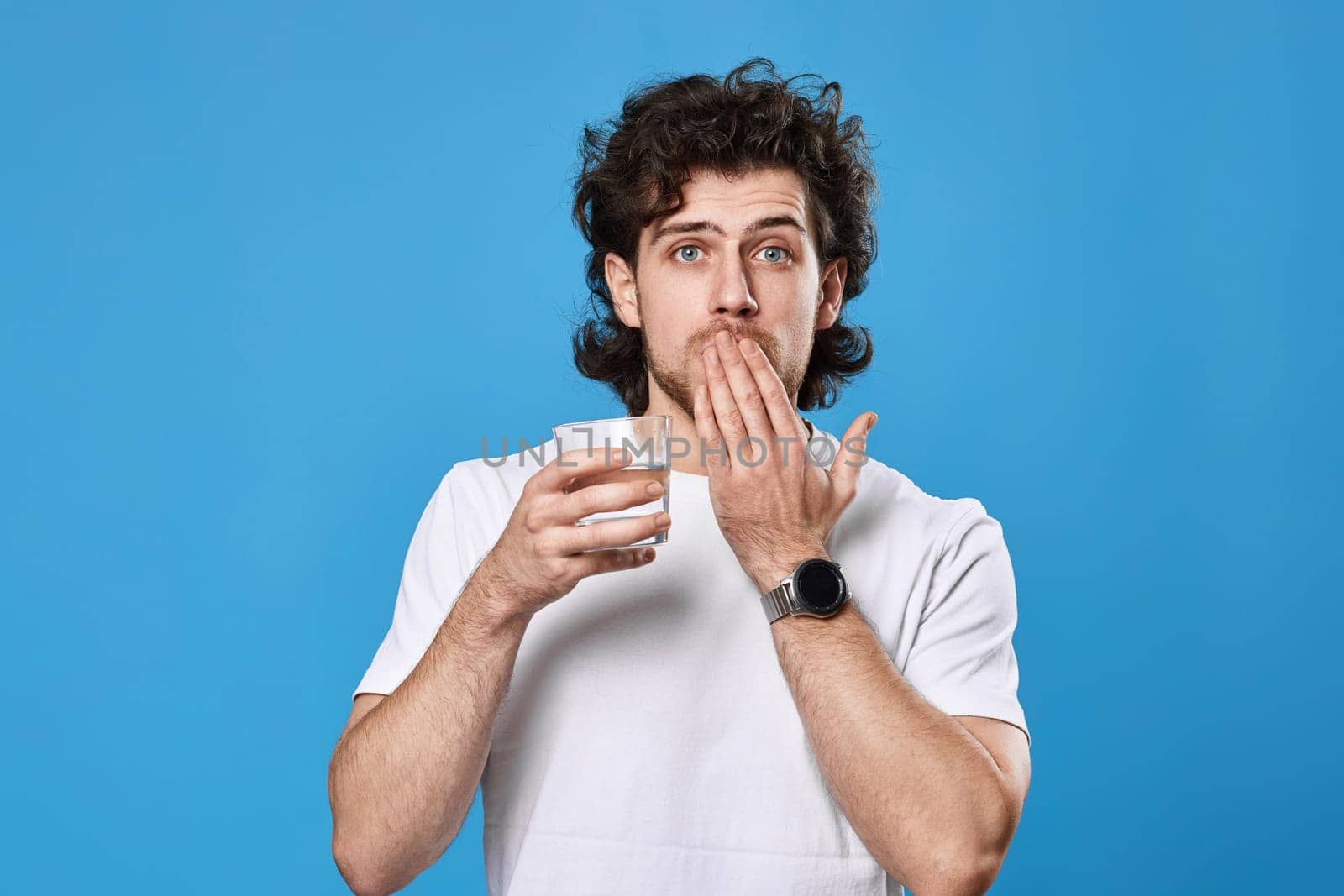 Young surprised handsome man with drinking glass of water on blue background
