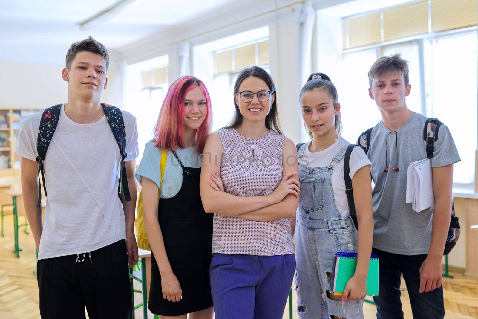 Group of teenagers pupils with young woman teacher, portrait of students and tutor in classroom, looking at the camera. Education, school, college, schoolchildren concept