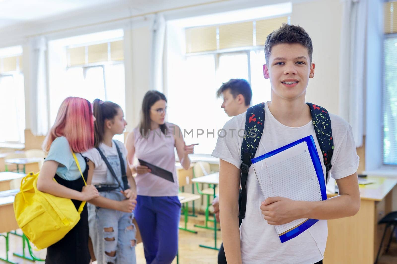 Portrait of teenage boy looking at camera, student boy in classroom with group of pupils children and female teacher. Education, school, college, teenagers concept