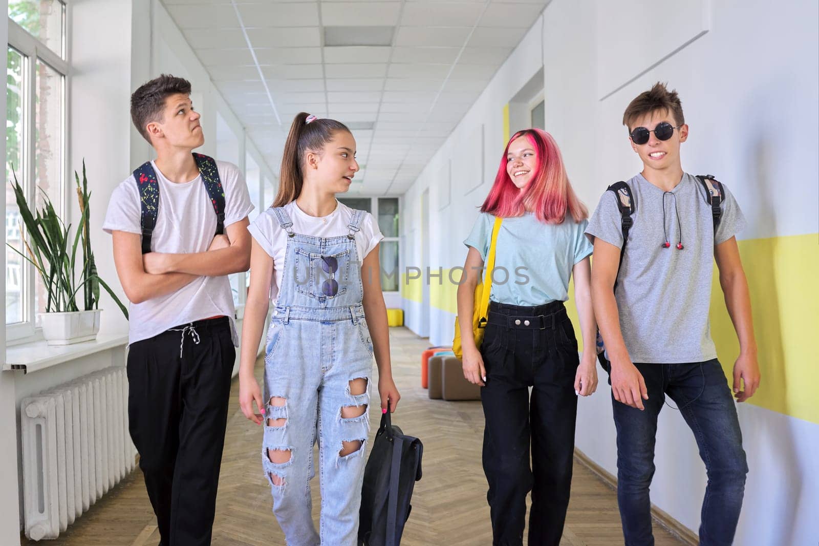Group of teenage students walking together along school corridor, schoolchildren smiling and talking. Education, high school, adolescence concept