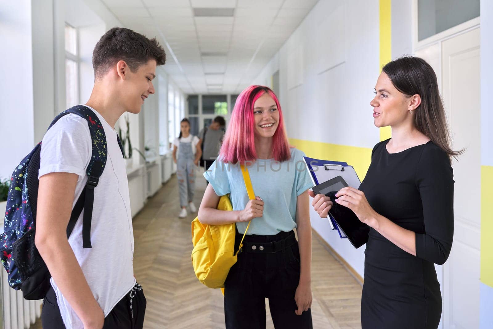 Group of teenage students talking to a female teacher in school corridor, smiling happy people. Teens, youth, school, college concept