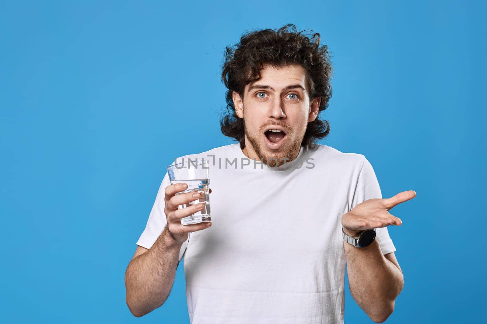 Young surprised handsome man with drinking glass of water on blue background