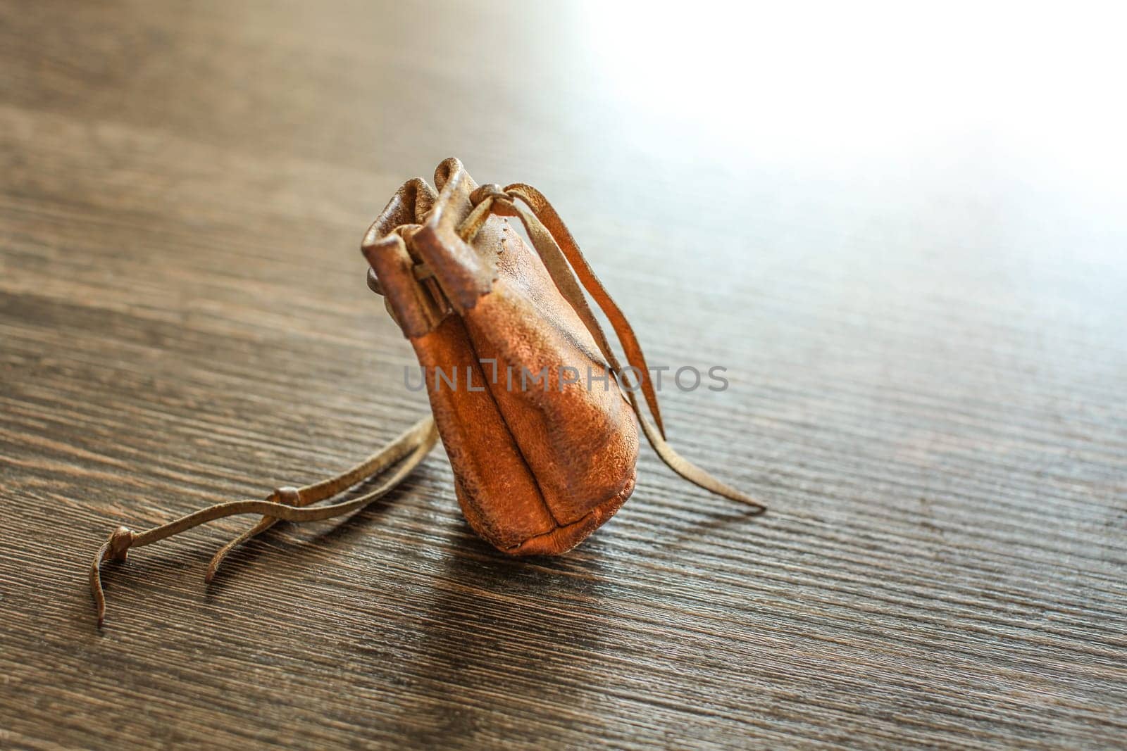 Old worn leather coin pouch on glossy wood desk, white light reflected in background.