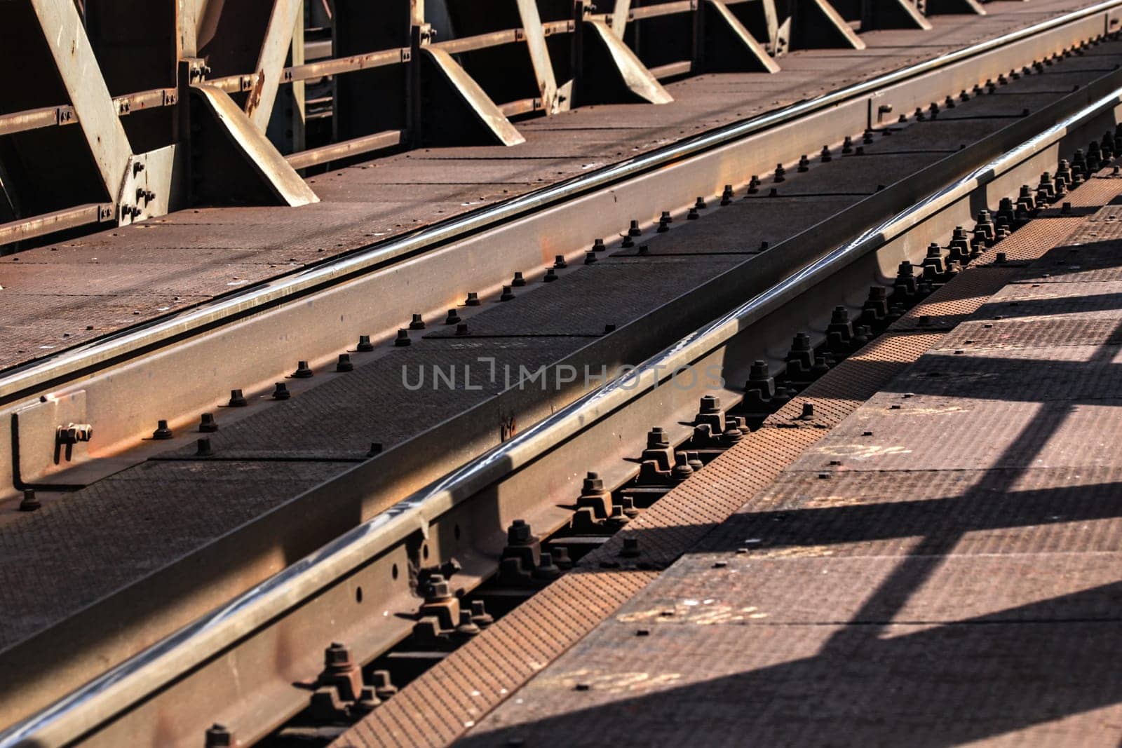 Detail of railway tracks on old metal bridge, sun casting shadows on them.