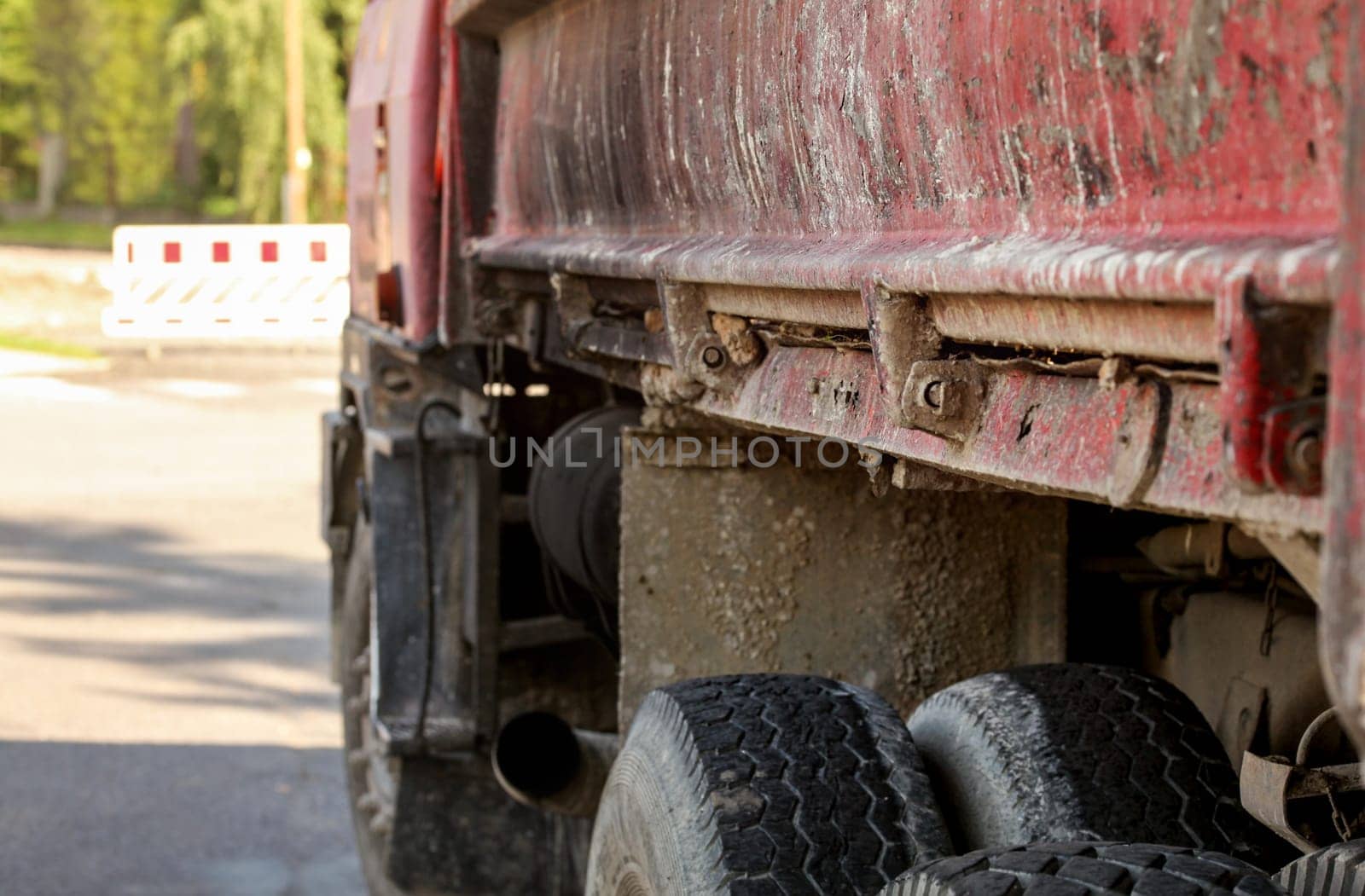 Closeup of old rusty and dirty truck side,  paint peeling on cargo area wall, large tires visible, blurred road block sign id distance. Roadworks illustration.