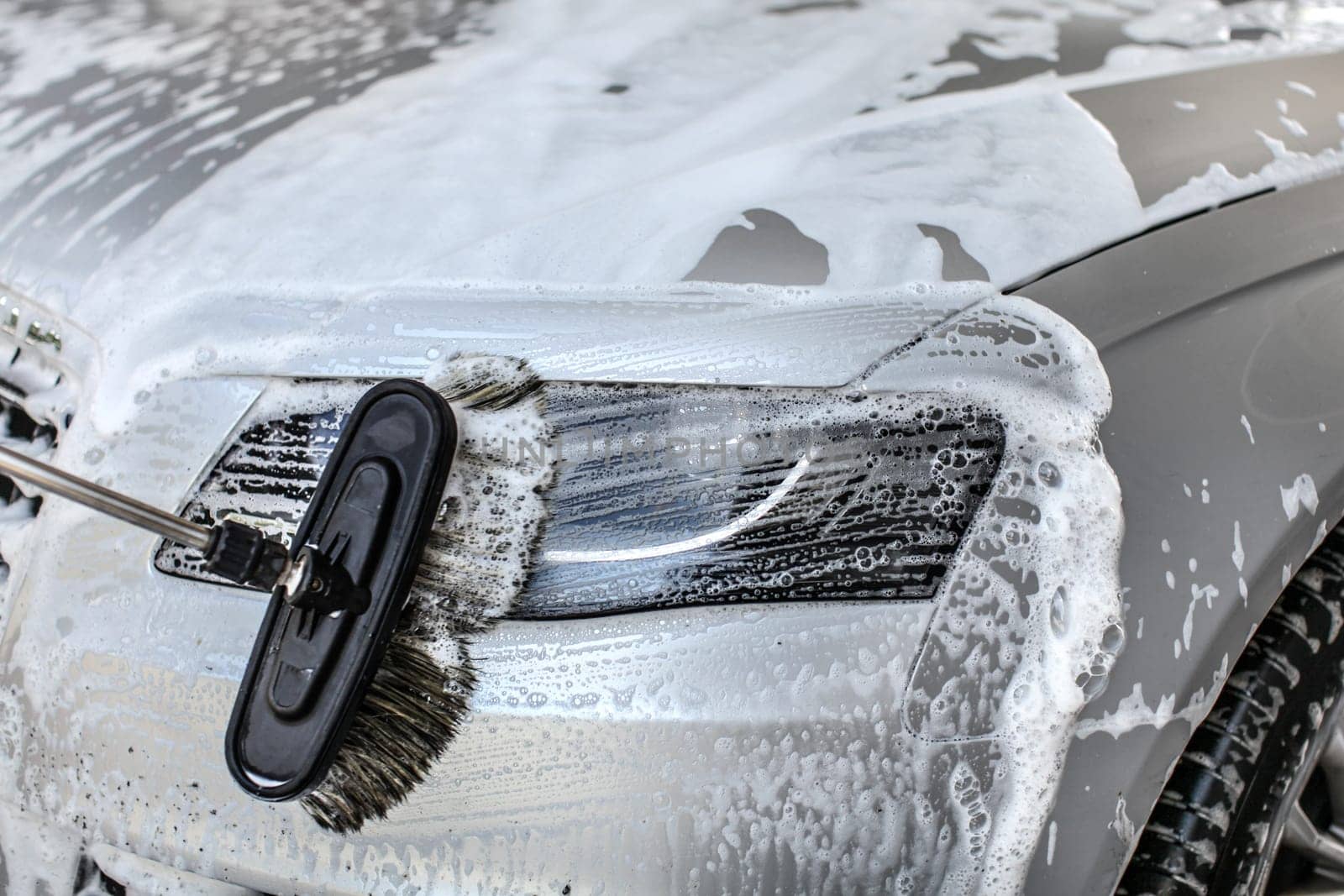 Car cleaned at manual carwash brush leaving strokes in shampoo on front light glass.