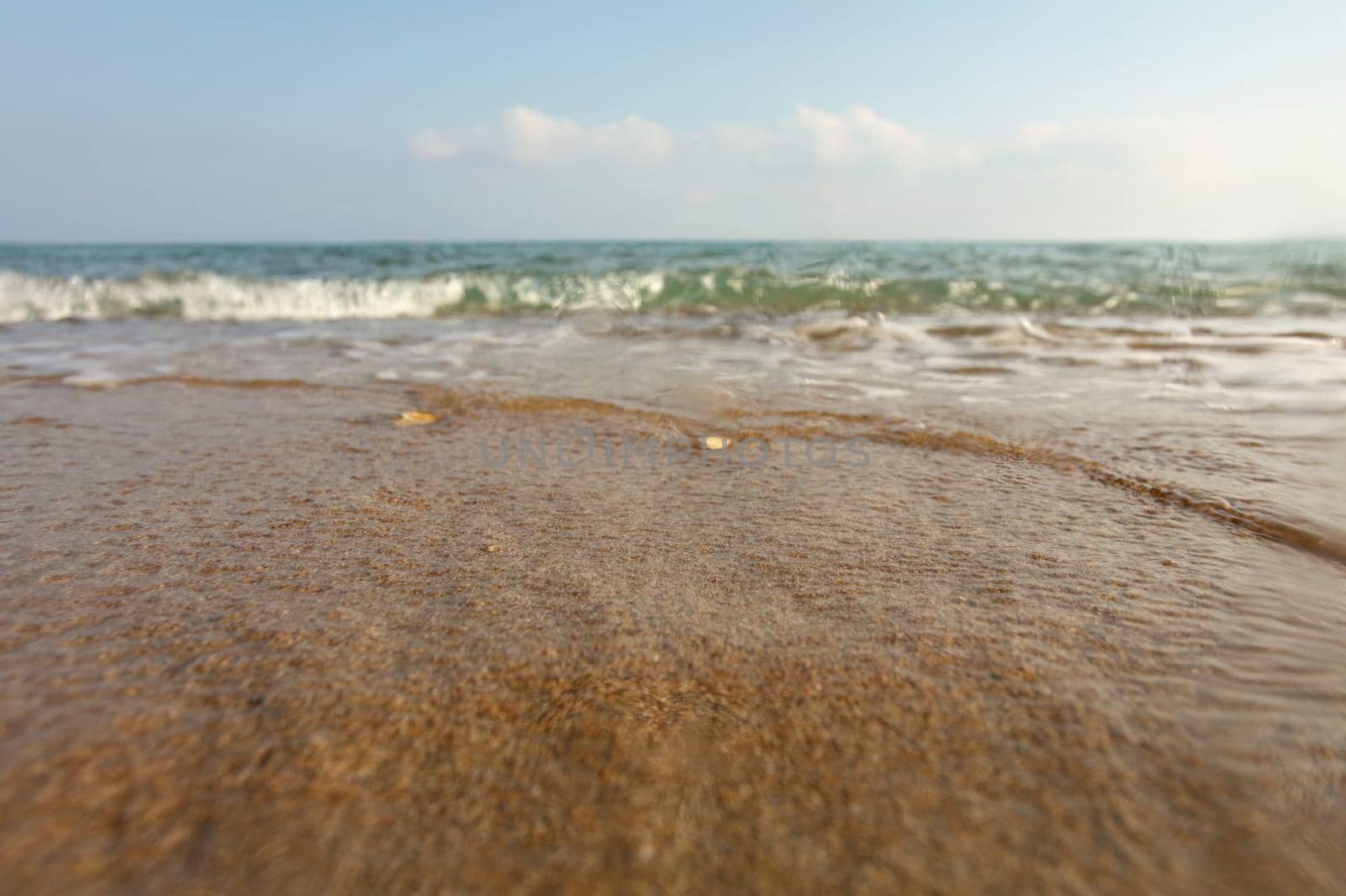 Wet sand on the beach, sea in distance, low angle photo on ground level, lens covered with some drops to emphasise water. Abstract marine background.