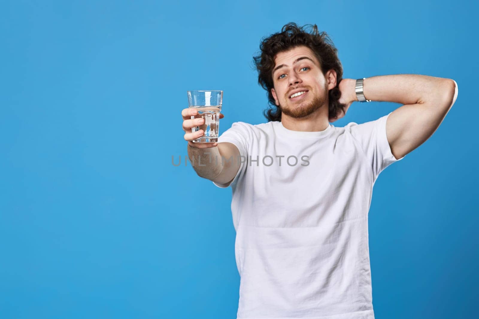 Young smiling handsome man offering a glass of water on blue background. focus on glass. copy space