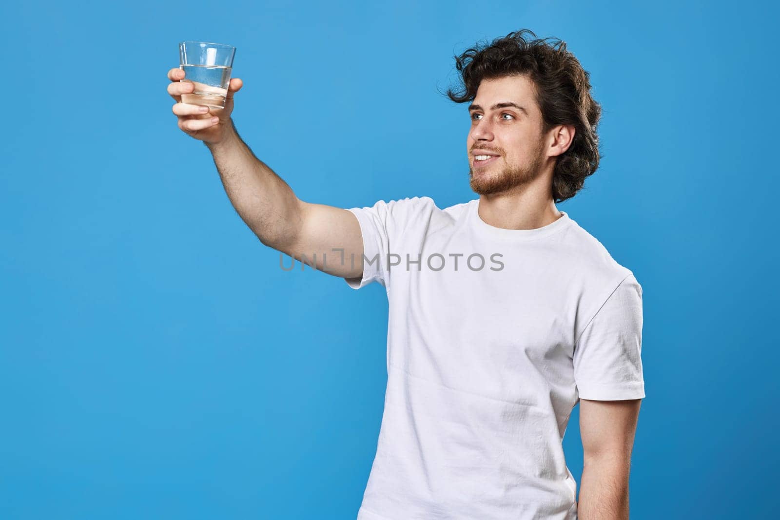 Young handsome man with drinking glass of water smiling happy on blue background