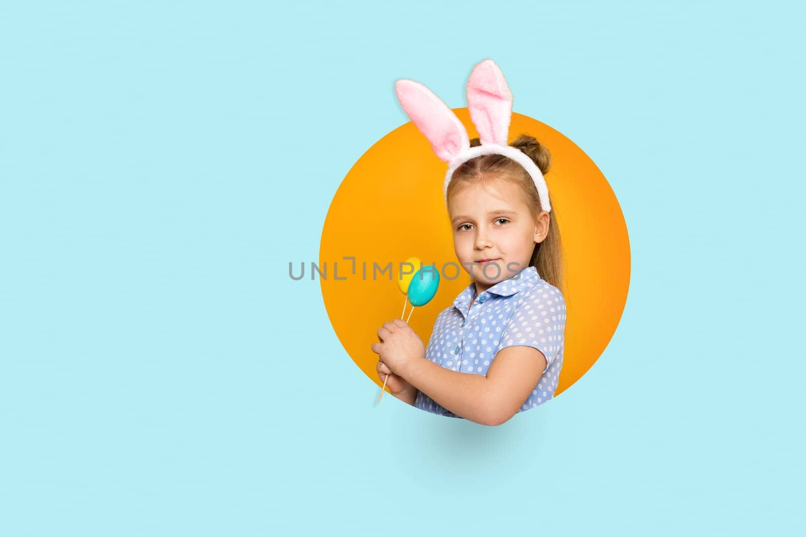 happy little child girl with Easter bunny ears holding colorful eggs on yellow and blue background. Happy easter. space for text