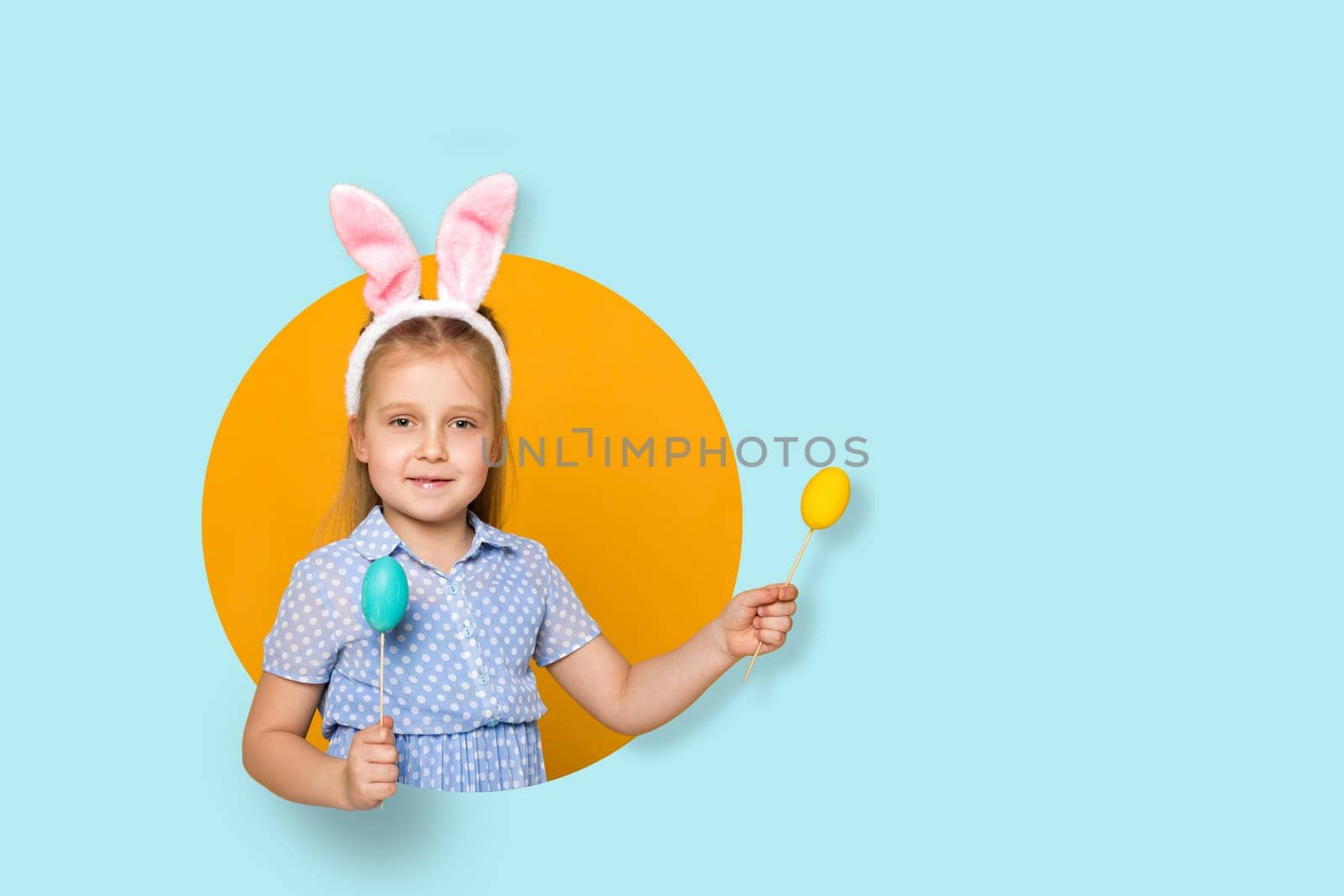 smiling little child girl with Easter bunny ears with colorful eggs on yellow and blue background. Happy easter. copy space
