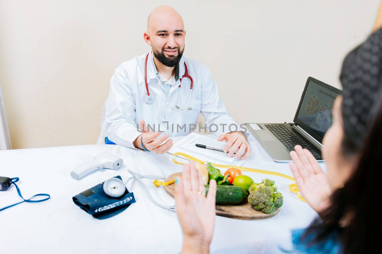 Nutritionist man talking to woman patient in office. Back view of a female patient talking to the nutritionist. Smiling nutritionist explaining to a female patient by isaiphoto