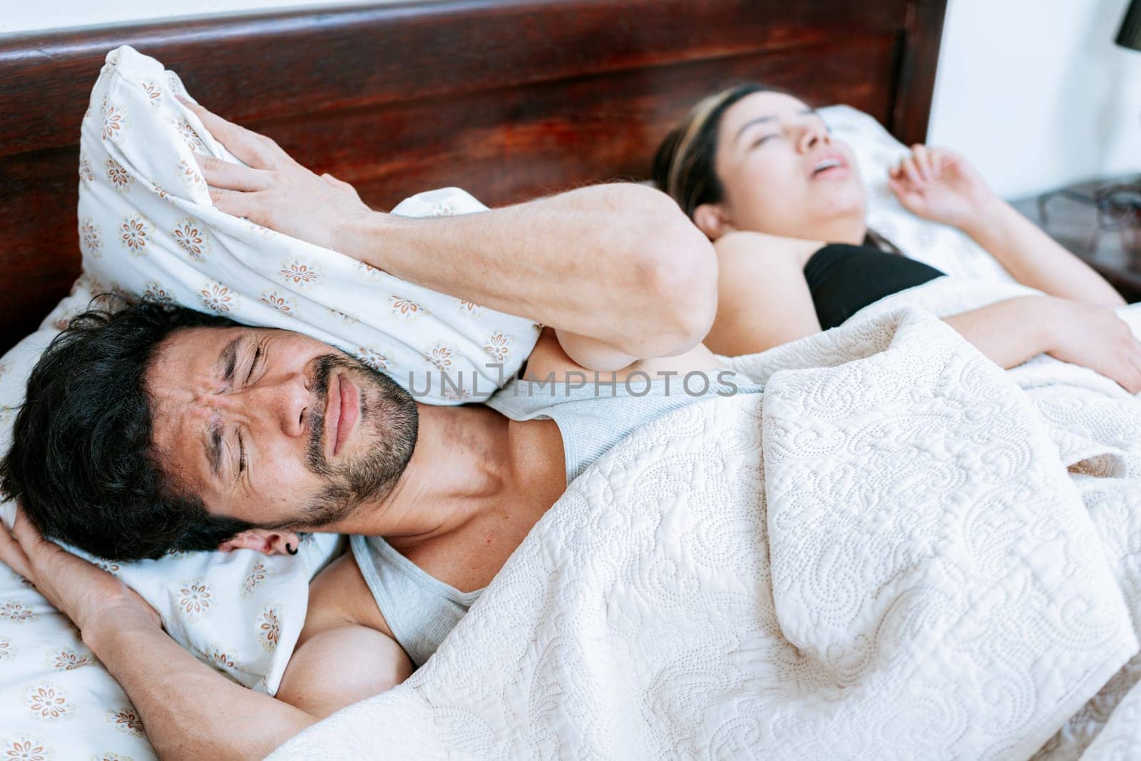 Woman snoring in bedroom and husband covering his ears. Husband suffering from the snoring of his sleeping wife. Sleep apnea concept