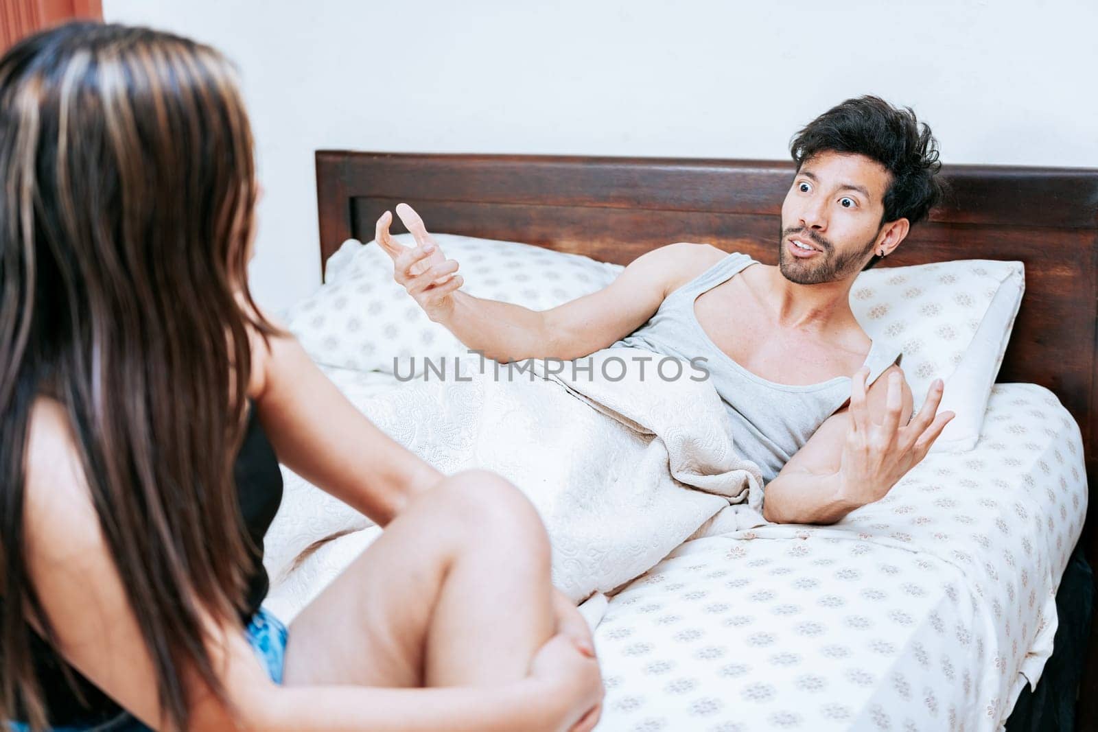 Young couple screaming at each other in bed. Husband arguing with his wife in bed, Concept of couple problems in bed. Upset woman with husband sitting on bed by isaiphoto
