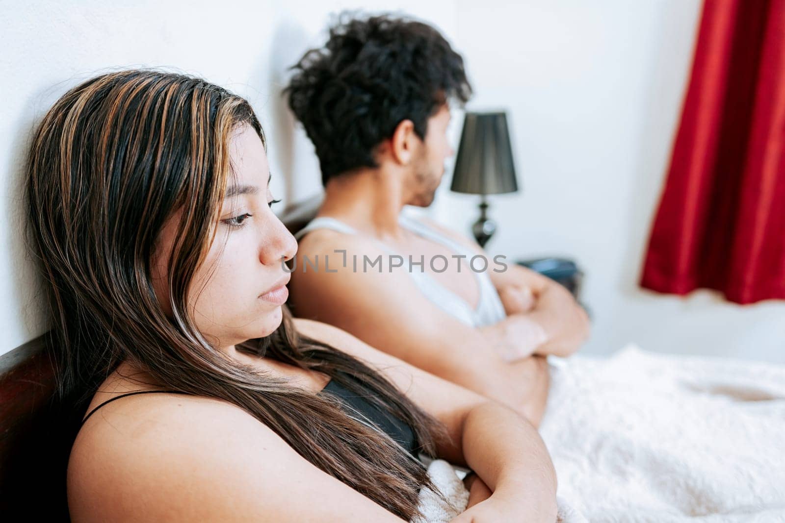 Concept of couple problems in bed. Upset woman with husband sitting on bed, Wife arguing with her husband in bed. Young couple arguing sitting on the bed by isaiphoto