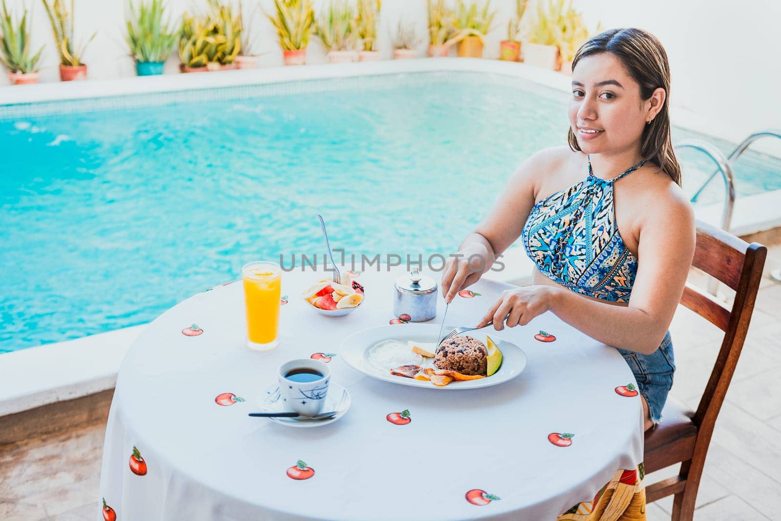 Smiling girl having breakfast near the swim pool. Woman on vacation having breakfast near swimming pool. Breakfast concept near swimming pool by isaiphoto