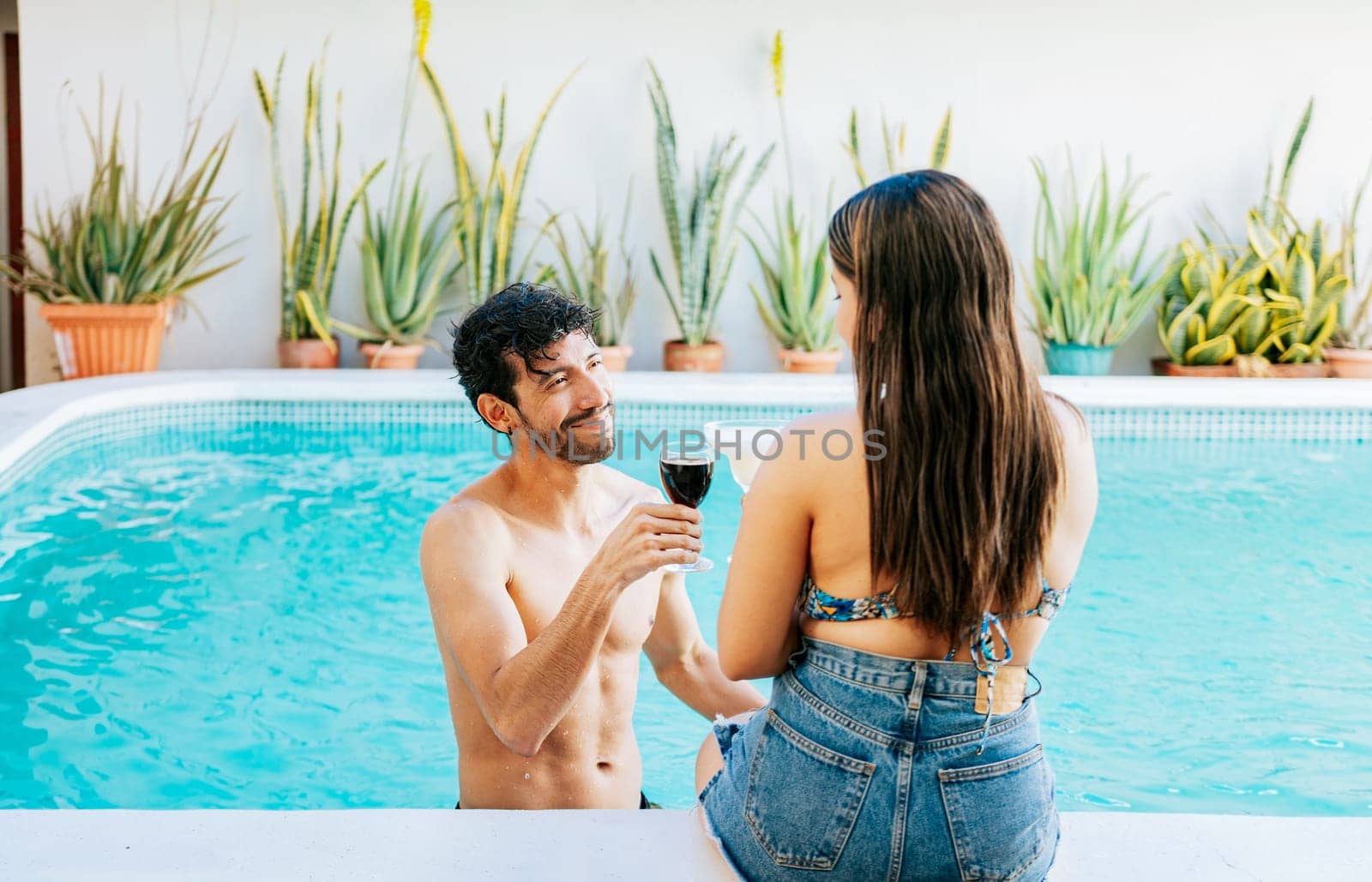 Happy couple on vacation toasting and talking in swimming pool, Smiling couple toasting in swimming pool. Young man and woman on vacation toasting in the pool by isaiphoto