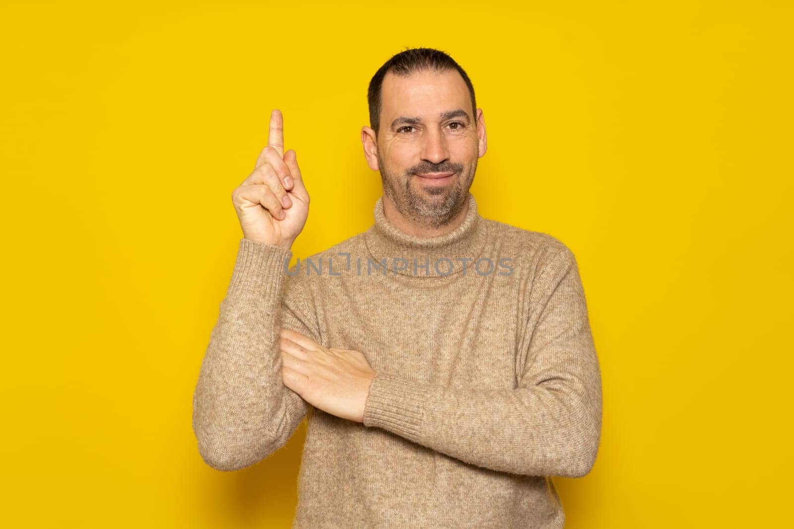 Bearded hispanic man wearing a beige turtleneck raising his index finger asking for a turn to express the great idea he had, he feels proud for having found a solution to the problem