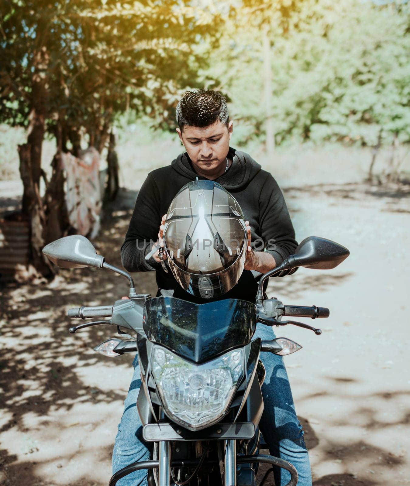 Biker motorcycle safety concept. Young motorcyclist man putting on safety helmet, Man on motorcycle putting on helmet. Motorcyclist putting on safety helmet by isaiphoto