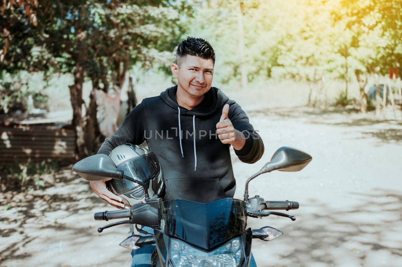 Biker on his motorbike holding safety helmet with thumb up. Concept of Smiling motorcycle cyclist holding safety helmet, Biker man giving thumb up while holding safety helmet