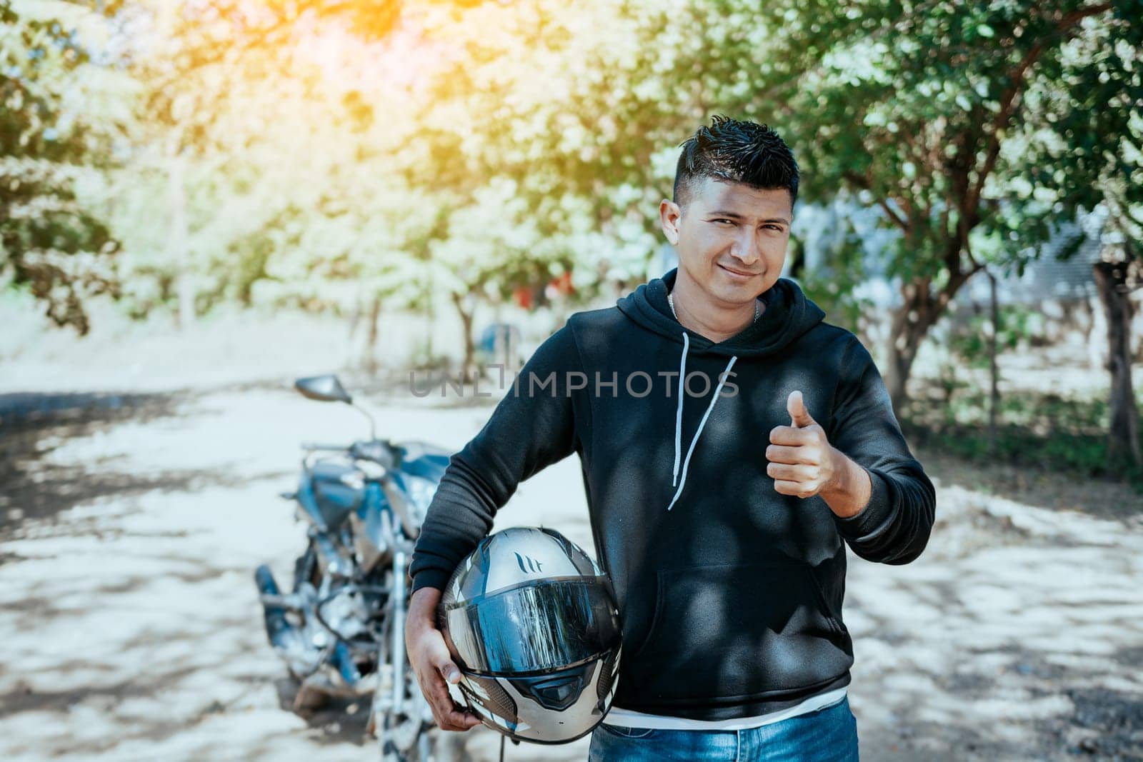 Portrait of motorcyclist holding safety helmet with thumb up. Smiling motorcyclist man holding safety helmet on the road. Motorcyclist giving thumbs up holding safety helmet on the road