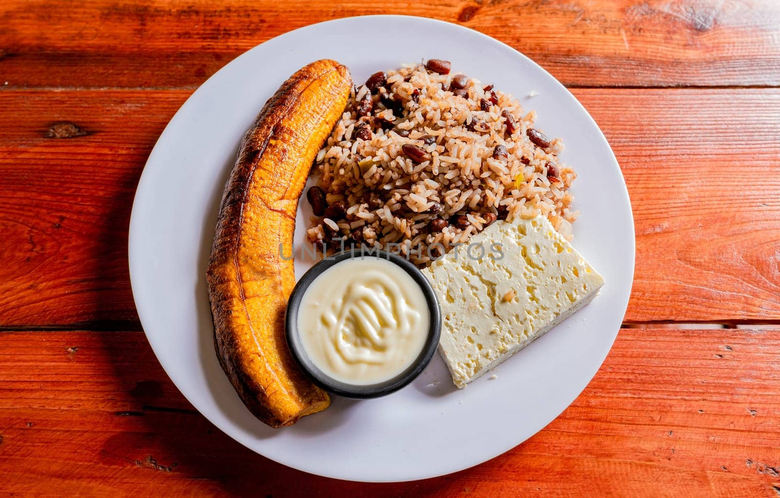 Gallopinto plate with cheese and maduro on wooden table. Nicaraguan food concept, Traditional Gallo Pinto meal with maduro and cheese served by isaiphoto