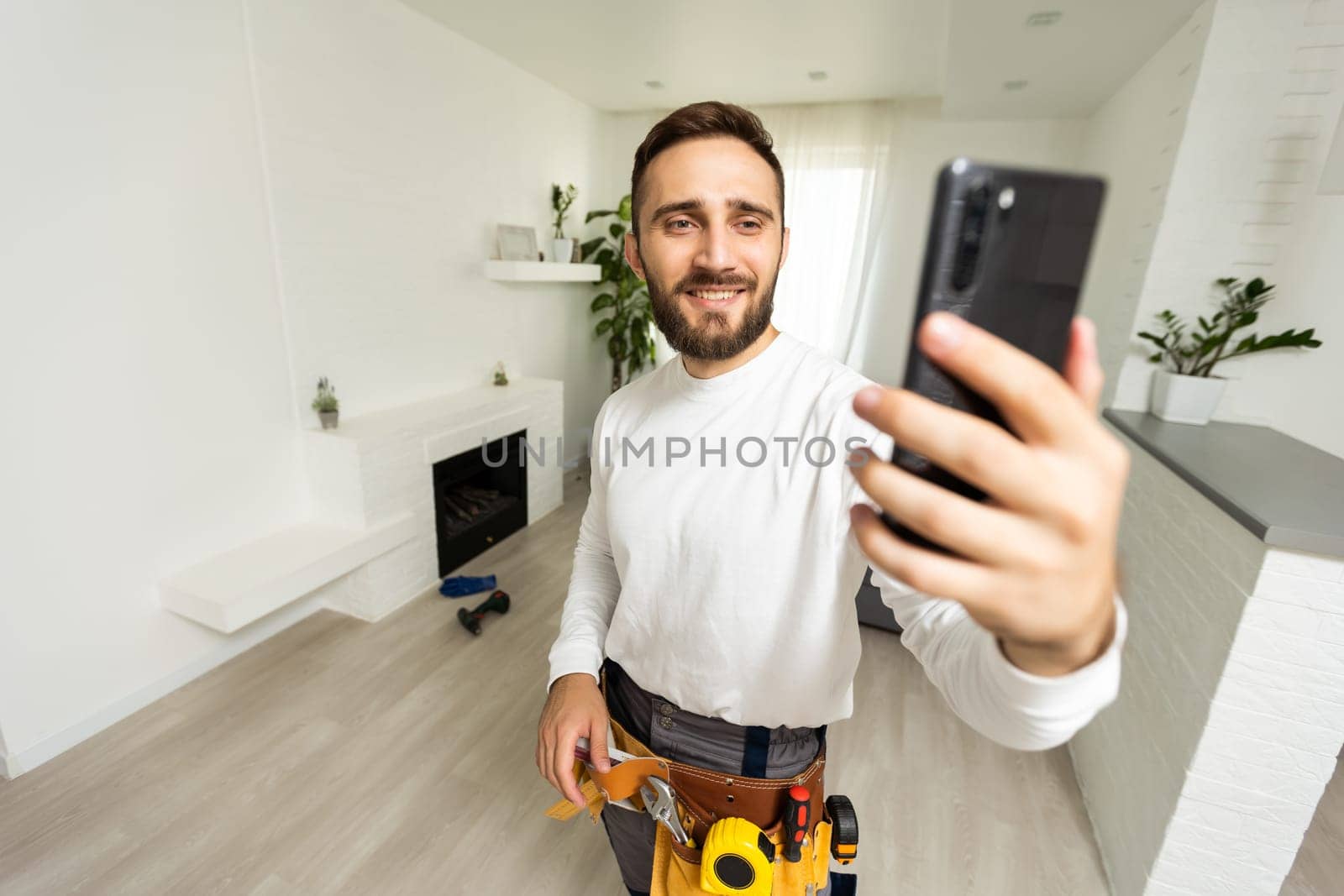 Smiling handsome young builder making selfie with mobile phone by Andelov13