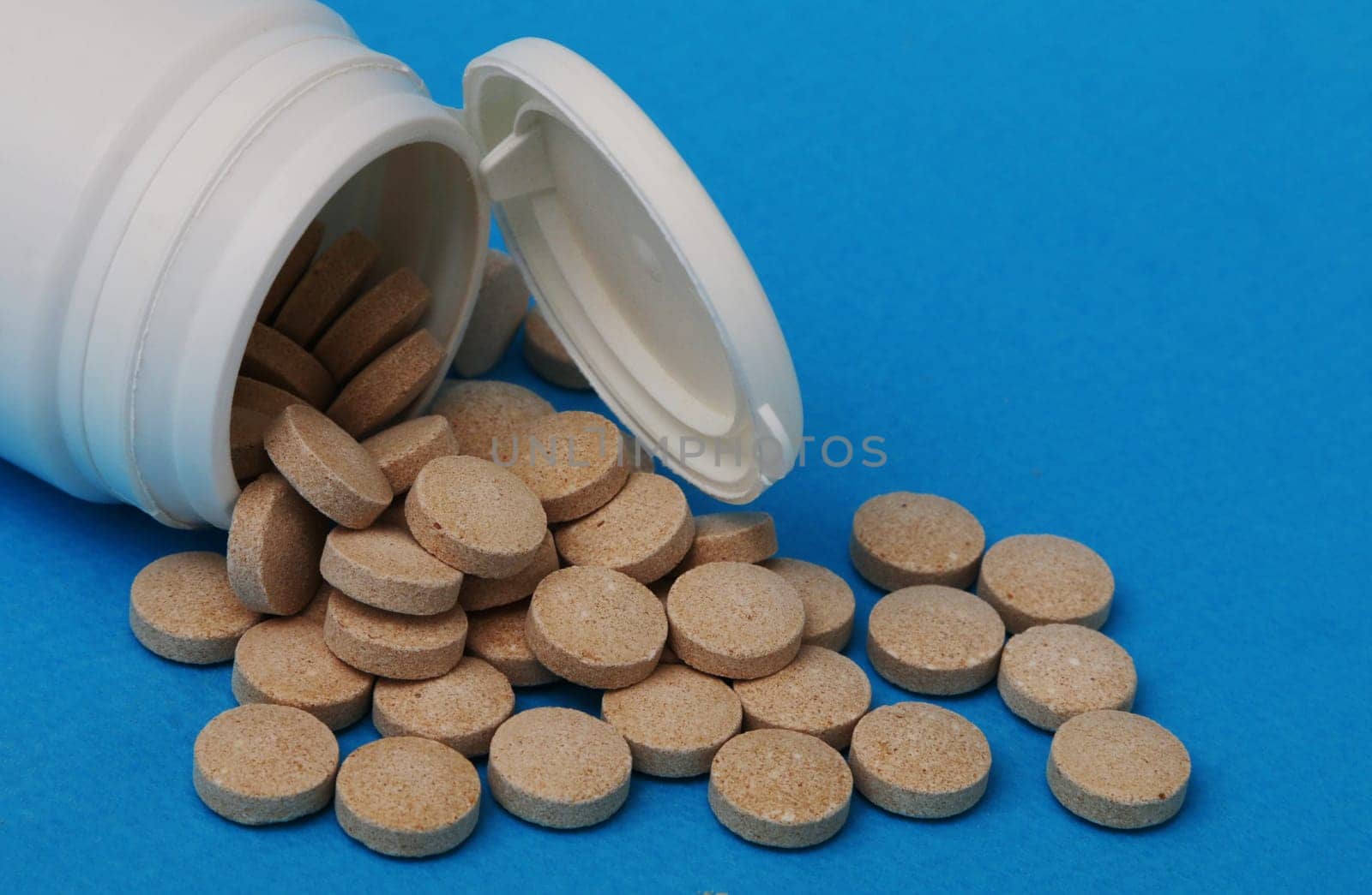 Medicine and health concept. Yellow-brown pills close-up. Pills spilled out from a white plastic bottle close-up.