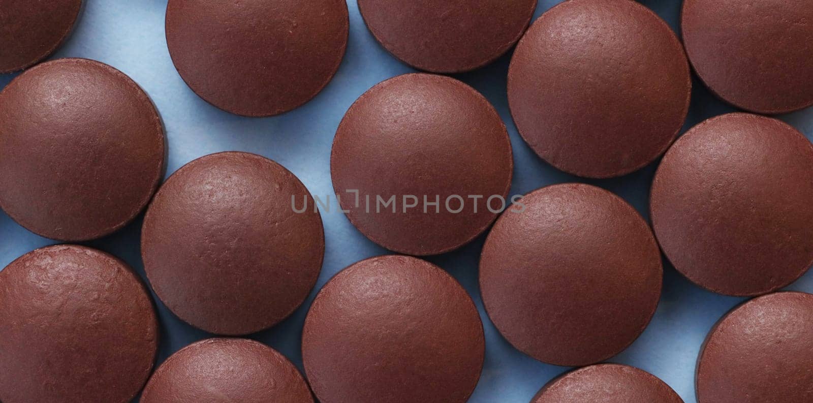 Close-up brown pills on a paper background in blue. Herbal supplements in the form of compressed tablets. Pharmaceutical concept.