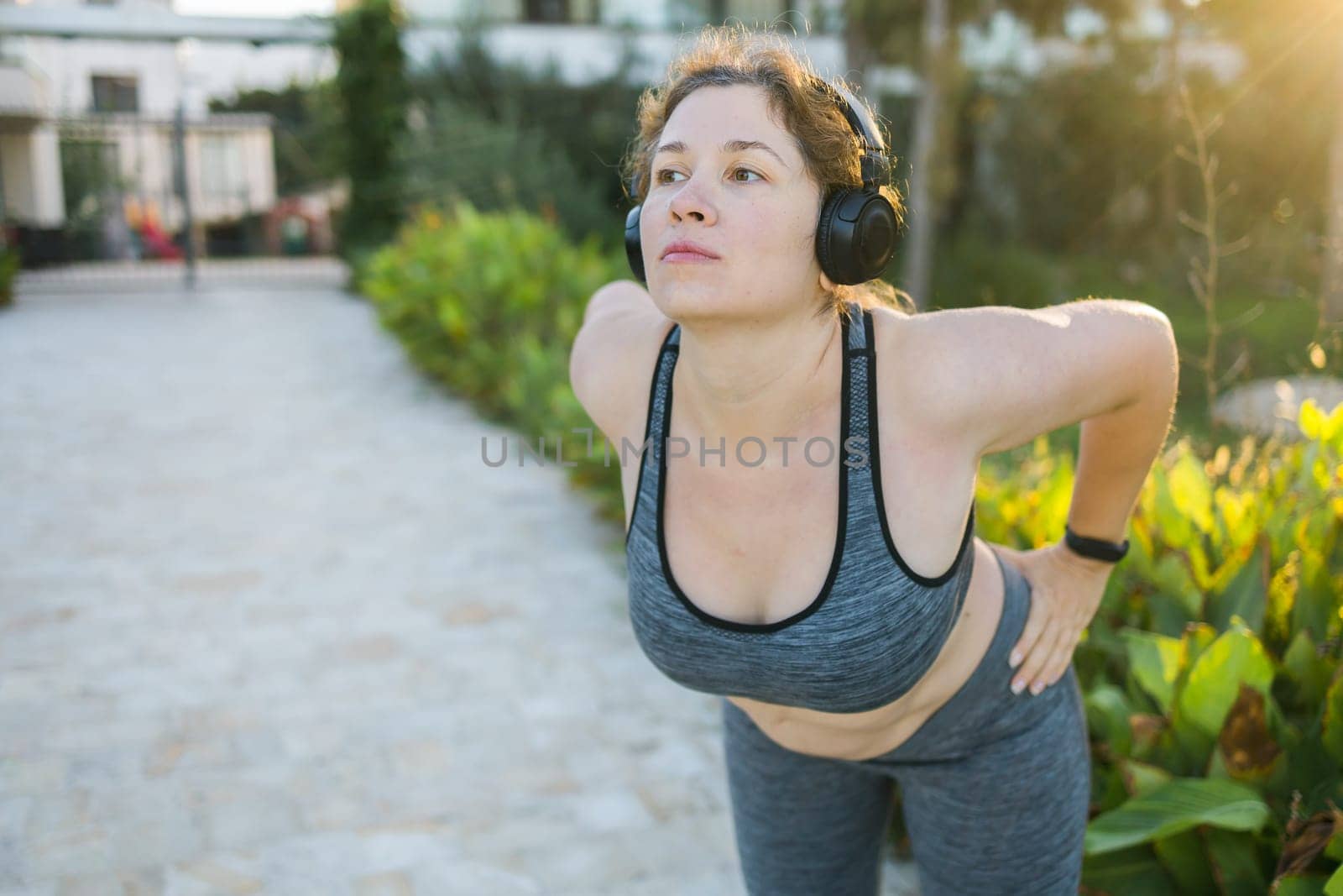 Young pretty smiling plus size woman in sporty top and leggings doing sport fitness and listen to music with headphones in summer morning outdoor copy space by Satura86