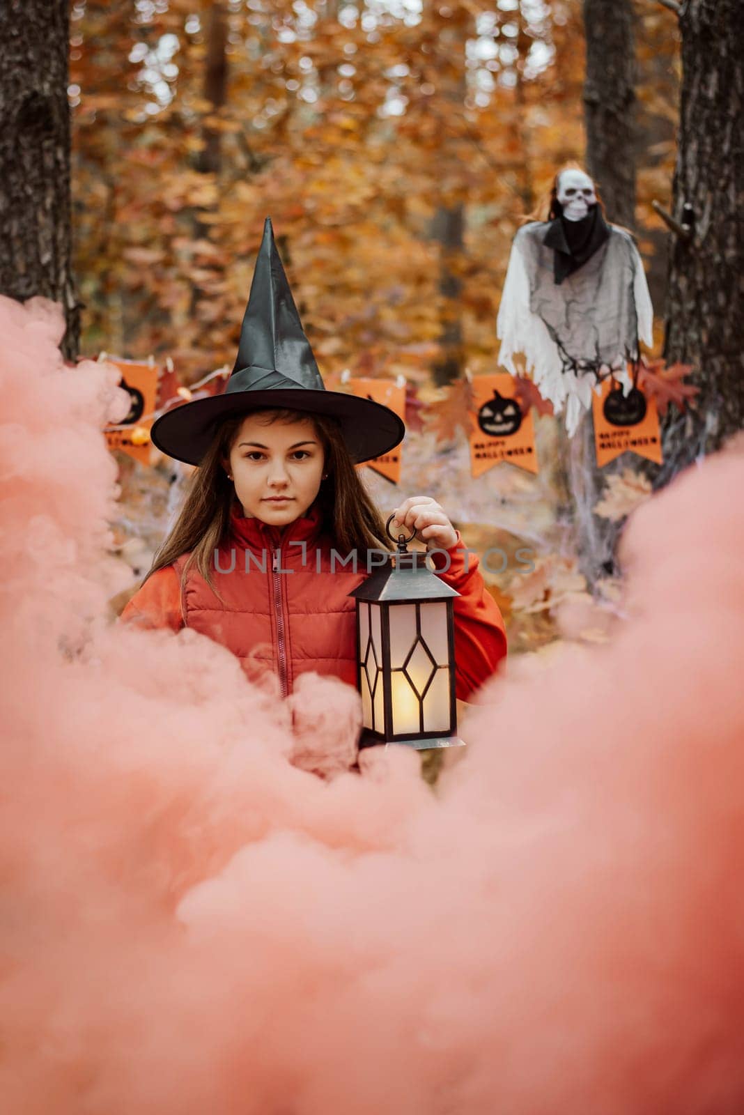 Little girl witch in black hat with lantern with a cloud of red smoke on the foreground